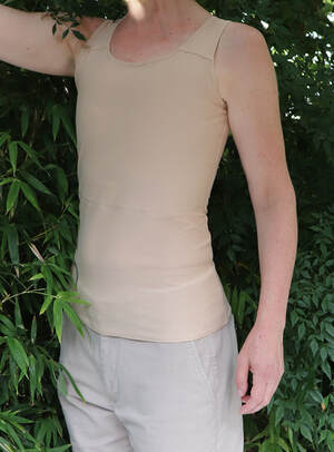 Person standing in front of a thick bamboo hedge wearing a Lily and Bang Bang skin tone long tank chest binder. We wanted to show in this photo how well the Milky Tea  colour way blends with a fair skin colour. The picture was taken by us in our suburban Sydney back yard 